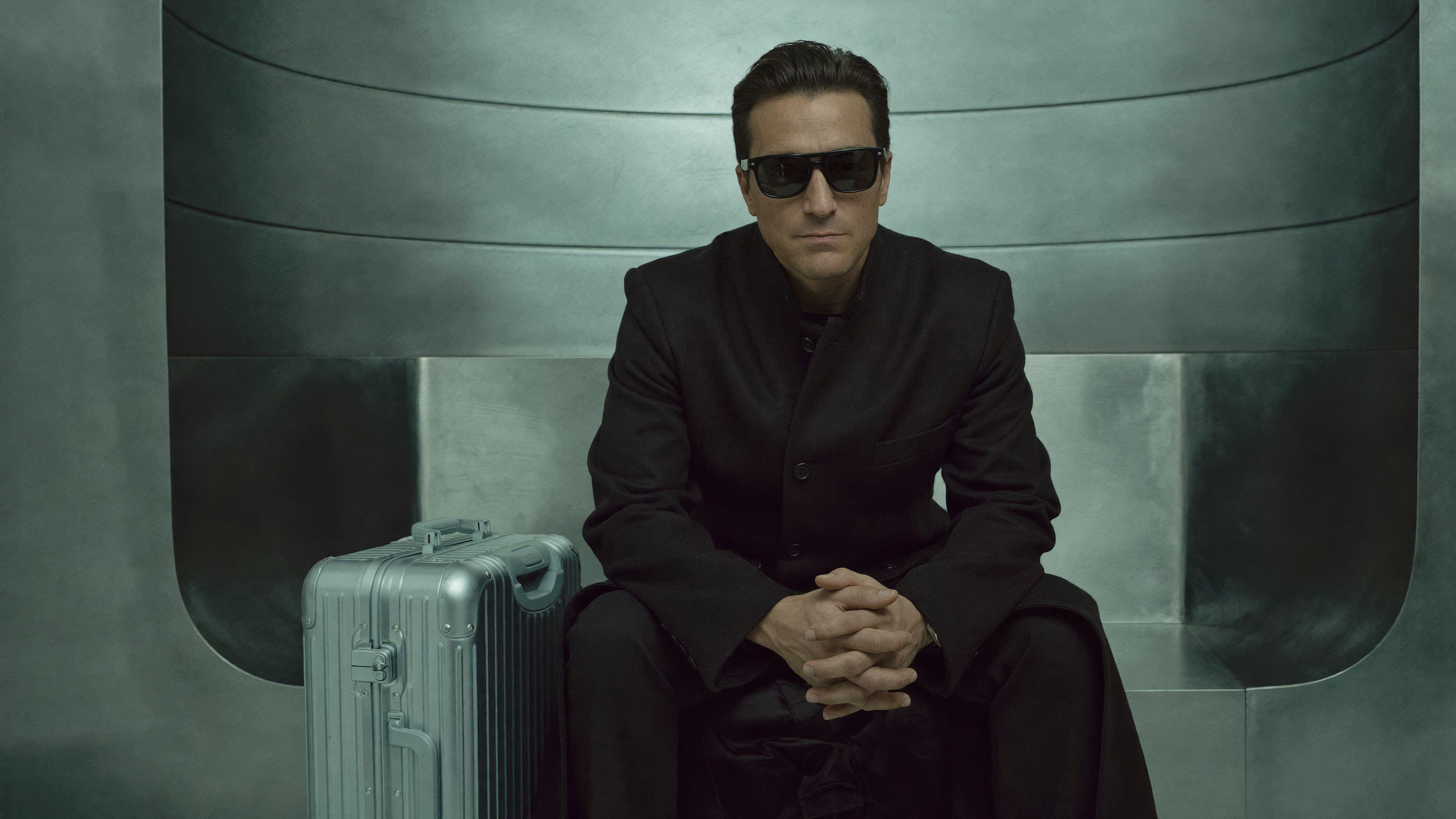 Blex seated beside a metallic case in a futuristic interior