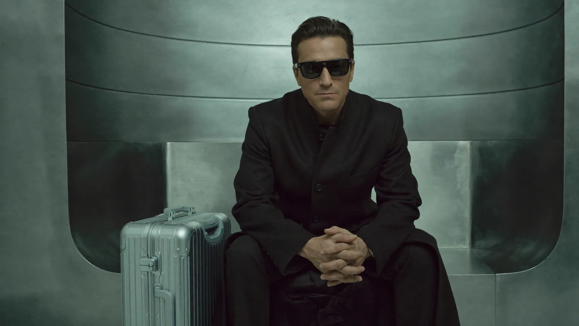 Blex seated beside a metallic case in a futuristic interior