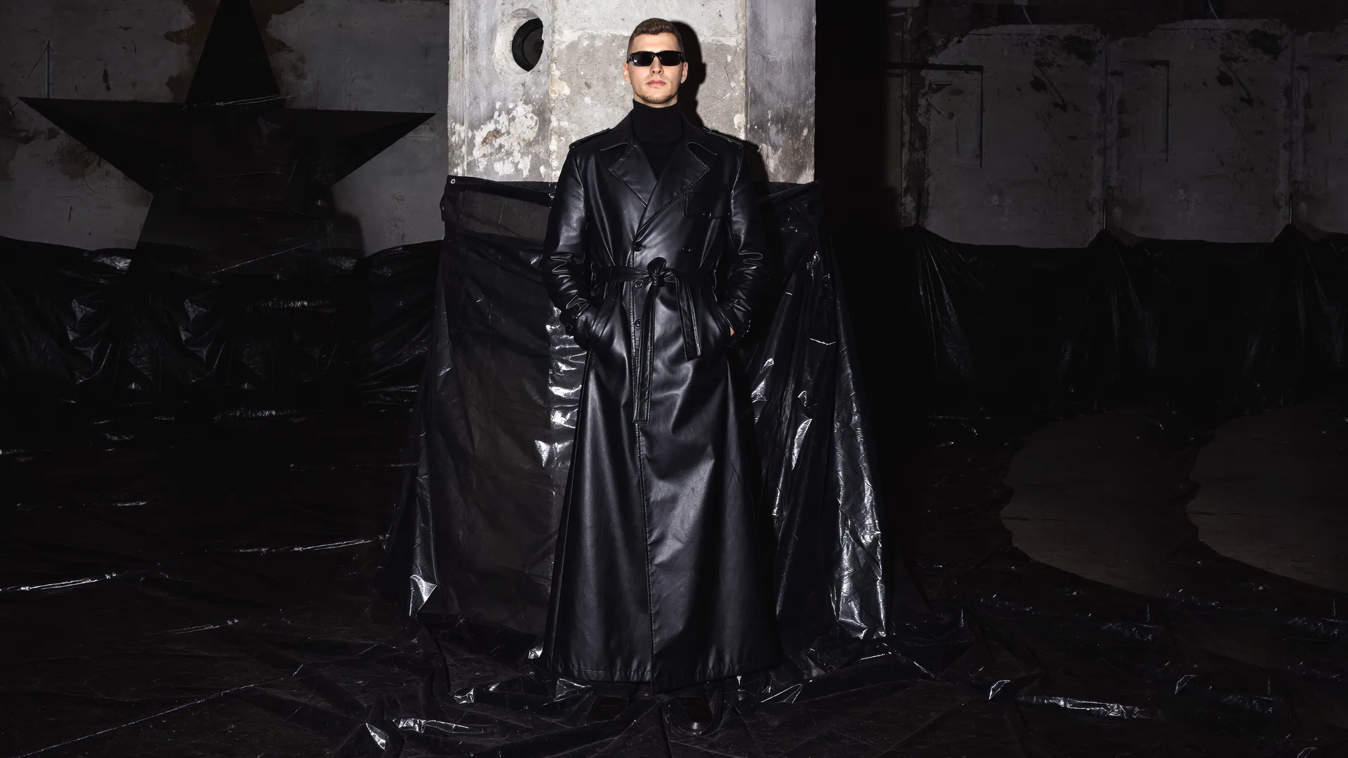 Ëlorian in a black leather silhouette within a raw architectural interior